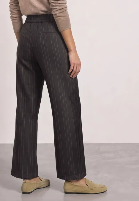 Straight Leg Hose mit Streifen und Schnalle black coffee Person von hinten in weiten, schwarzen Nadelstreifenhosen und beigen Loafers, Oberteil in hellen Tönen.