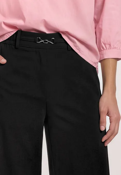 Zwarte wijduitlopende broek met riem en roze blouse, alleen de romp vanaf de taille zichtbaar.