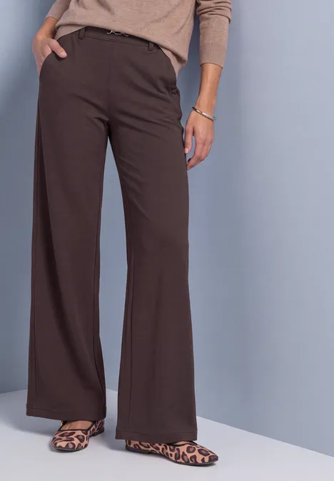 High Waist Straight Leg Hose im Casual Fit ruby vine Braune, weit geschnittene Damenhose mit Leopardenmuster-Schuhen vor grauem Hintergrund.