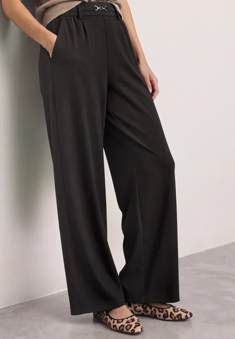Zwarte, wijde, hoog getailleerde broek met zijzakken en riem, gecombineerd met luipaardprint instappers.