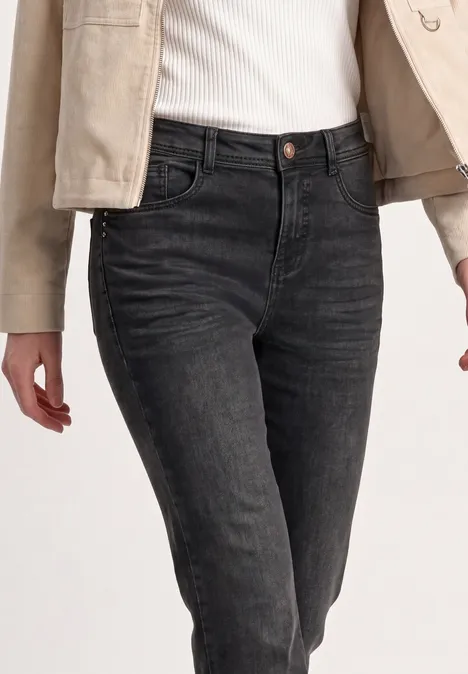 Dunkle, eng geschnittene Damenjeans mit hohem Bund, kombiniert mit weißem Top und hellbeiger Jacke.