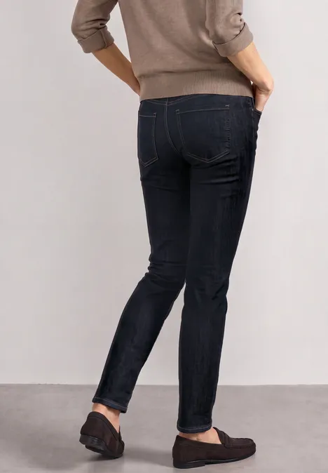 Dżinsy z Mid Waist i wąskimi nogawkami o Casual Fit Deep Rinse Washed Kobieta w czarnych obcisłych dżinsach i ciemnych mokasynach, stojąca bokiem z rękami w kieszeniach.