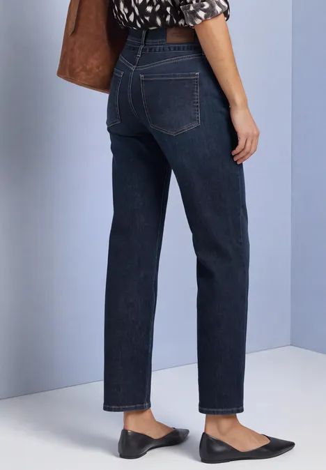 Frau trägt dunkle, gerade geschnittene Jeans und schwarze Ballerinas, nur der Unterkörper ist sichtbar.