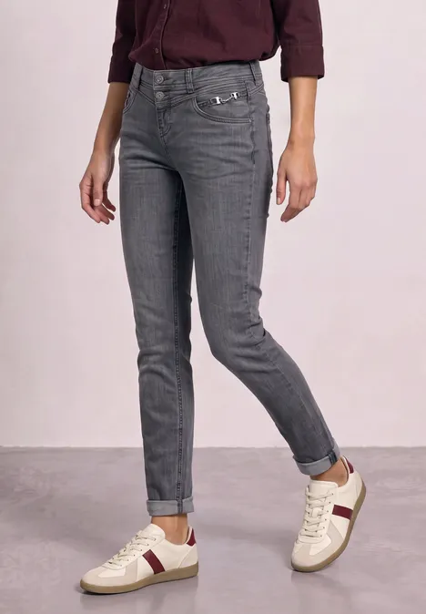Graue Jeans kombiniert mit weißen Sneakers und einem burgunderfarbenen Oberteil.