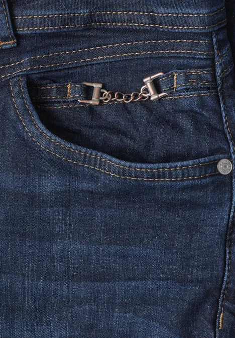 Nahaufnahme einer blauen Jeans mit dekorativer silberner Kette am vorderen Hosentaschensaum.