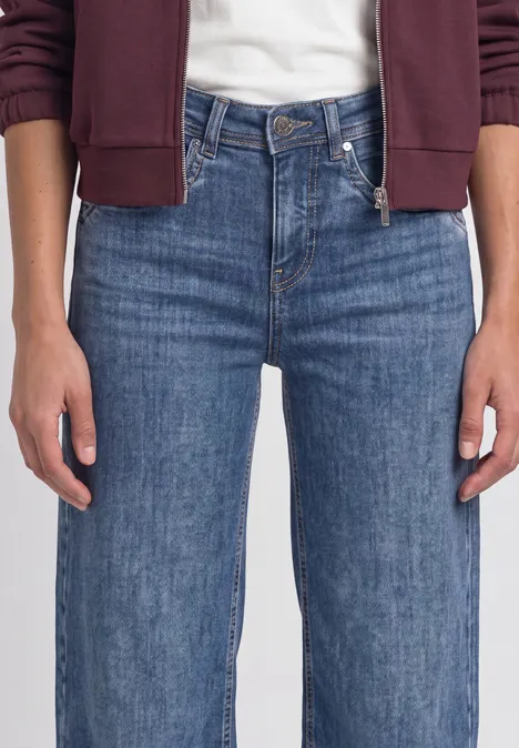 High Waist Wide Leg Jeans im Loose Fit Medium Blue Soft Washed Frau trägt blaue Jeans und weinroten Hoodie, Hände locker seitlich am Körper.