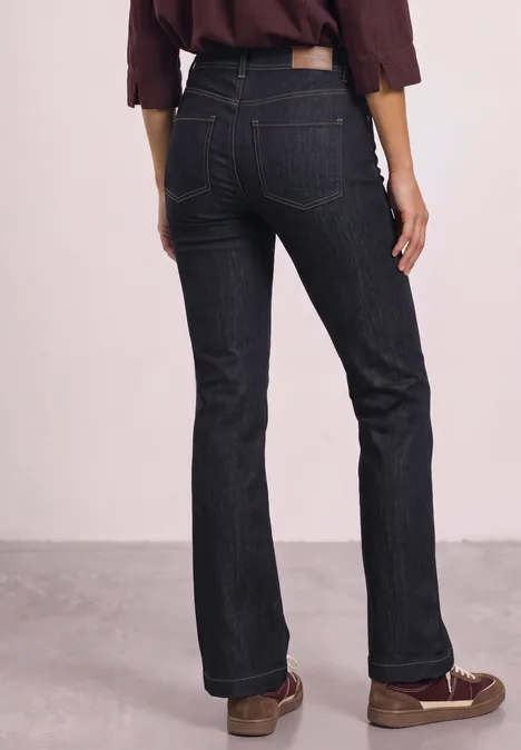 High Waist Bootcut Jeans im Slim Fit Rinse Soft Washed Frau von hinten in hoch taillierter, dunkler Jeans und braunen Loafers vor neutralem Hintergrund.