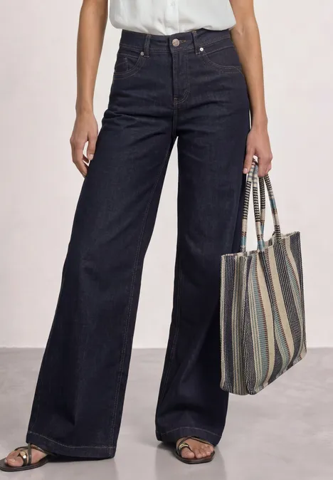 Dunkle, hoch geschnittene, weite Jeans kombiniert mit offenen Sandalen und einer gestreiften Stofftasche.