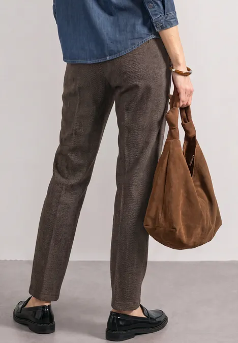 Frau trägt dunkle Hose, schwarze Loafers und eine braune Velourstasche, gesehen von hinten