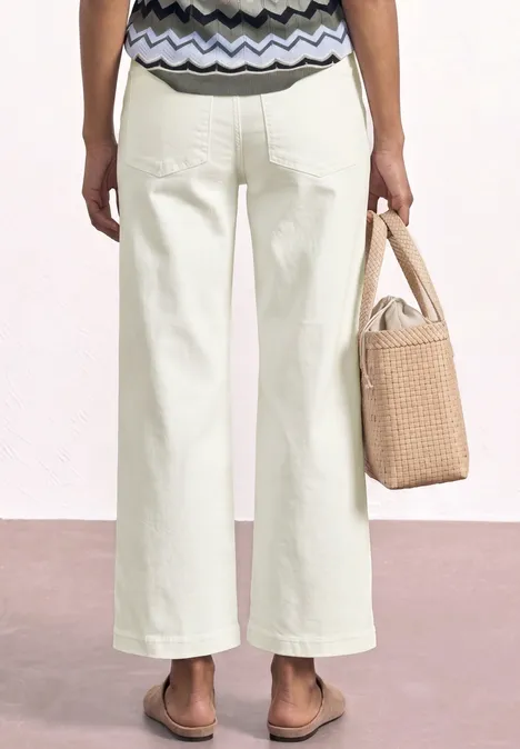 Frau von hinten in weißen Schlaghosen, gemusterter Bluse, Sandalen und Strohtasche