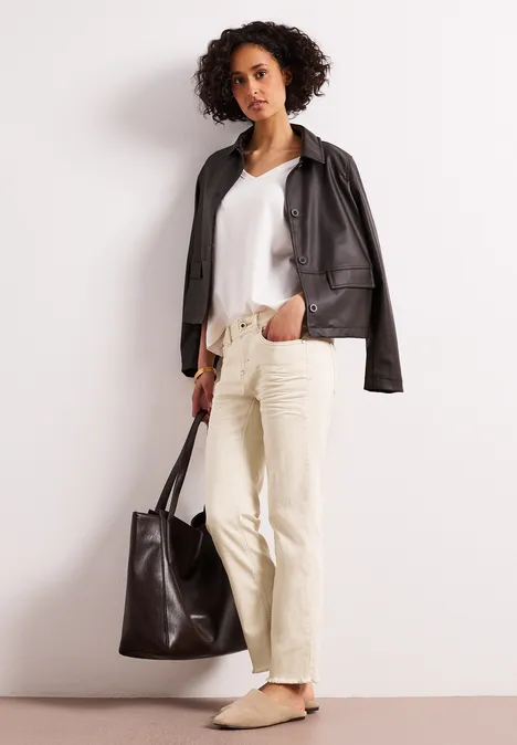 Persoon met zwarte leren jas, wit topje, beige broek en grote zwarte tas.