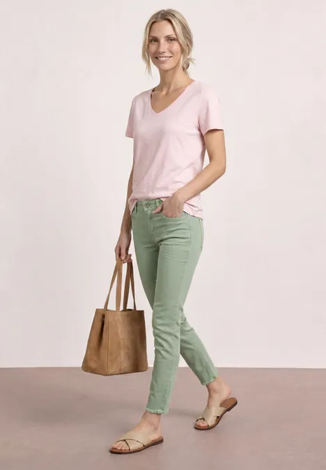 Frau trägt rosa T-Shirt, grüne Hose, Sandalen und hält eine braune Tasche.