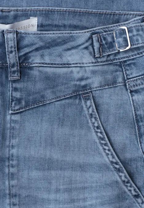 Blauer Jeansstoff mit Tasche, Bund und seitlicher Schnalle in Nahaufnahme.