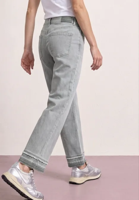 Persoon van achter gezien in losse grijze jeans en zilverkleurige sneakers, casual stijl.