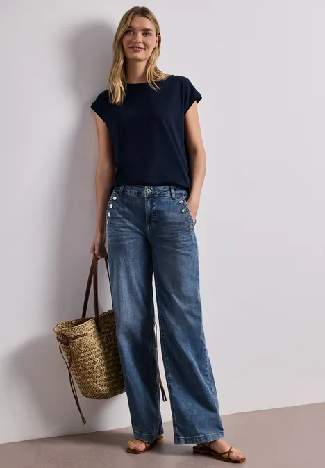 Femme en t-shirt bleu marine, jean ample, sandales plates, tenant un panier en osier.