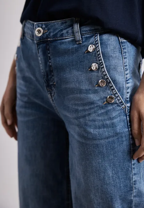 Jean bleu avec fermeture boutonnée latérale et boutons argentés, coupe décontractée.