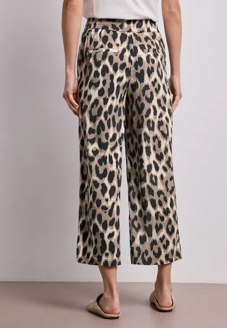 Weite, knöchellange Hose im Leopardenmuster, kombiniert mit einfachen Sandalen vor neutralem Hintergrund.