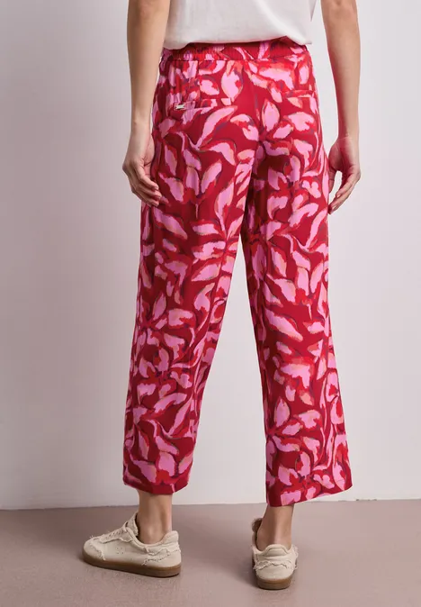 Een persoon van achteren draagt een wijde rode broek met roze bladmotief.