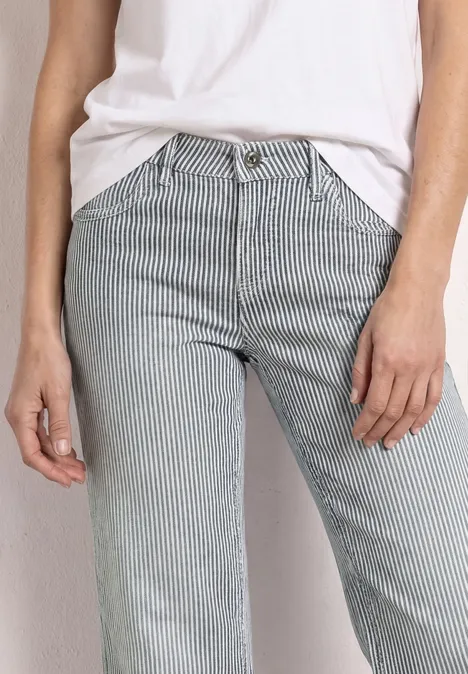 Person in weißem Oberteil und hellgrauer Hose mit feinen vertikalen Streifen