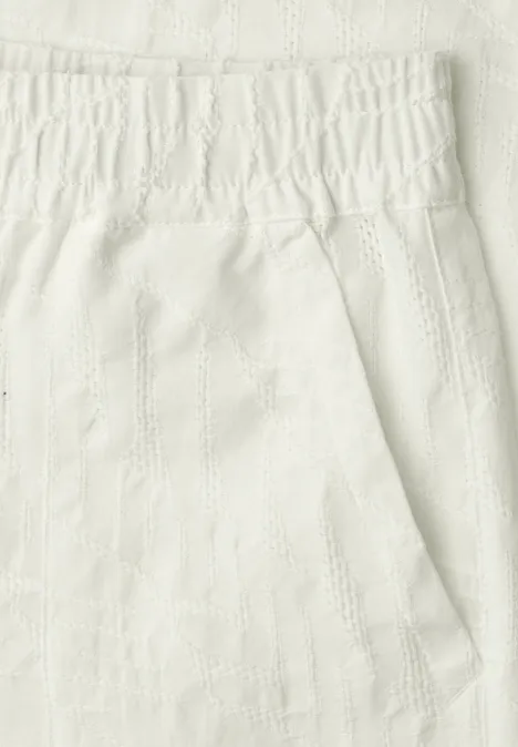 Close-up van een witte, gestructureerde stof met elastische tailleband en een zak