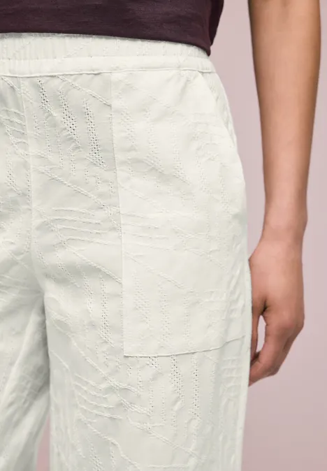 Persoon draagt lichte, doorgestikte patchworkbroek en een bordeauxrood bovenstuk.