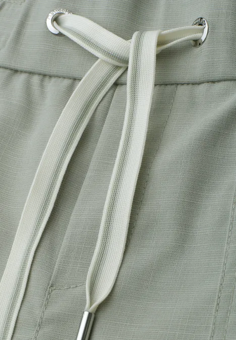 Close-up van lichtgroene broek met witte trekkoord in de taille.