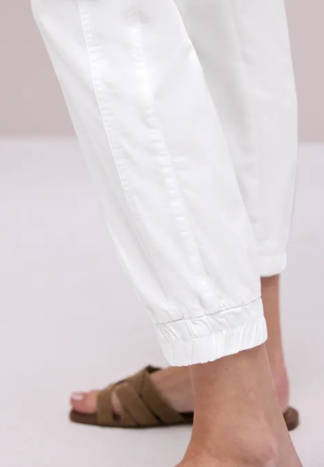 Enkel en voet in witte joggerbroek met bruine slip-ons