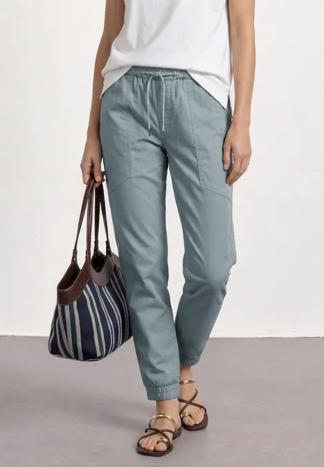 Slim legs broek in lichtgewicht kwaliteit washed blue Vrouw draagt witte top, lichtblauwe broek, gestreepte tas en sandalen.