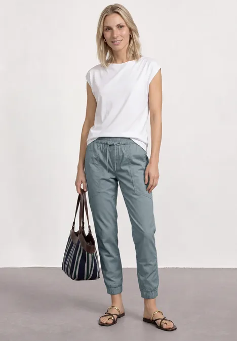 Slim legs broek in lichtgewicht kwaliteit washed blue Een vrouw in een wit topje en grijsblauwe broek met gestreepte tas.