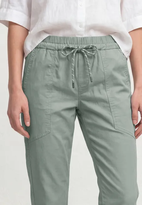 Slim legs broek in een lichtgewicht stof dark mint green Frontal beeld van iemand in een lichtgroene cargobroek met elastische taille en een los witte blouse.