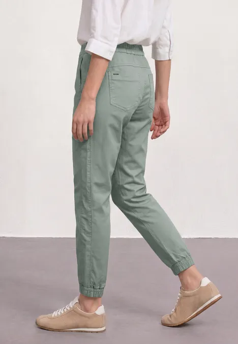 Slim legs broek in een lichtgewicht stof dark mint green Persoon draagt saliegroene, comfortabele broek met elastische zoom, witte top en beige sneakers.