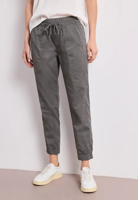 Persoon draagt een grijze, losse broek met trekkoord en witte sneakers.