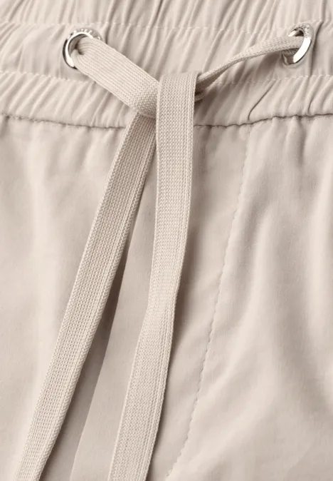 Close-up van een beige broek met tunnelkoord.