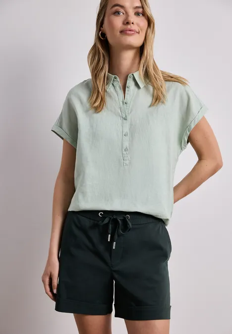 Person in hellgrünem Kurzarmhemd und schwarzen Shorts vor hellem Hintergrund