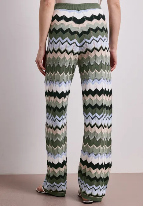 Persoon van achteren in wijde zigzaggebreide broek in groen, blauw en zwart met sandalen.