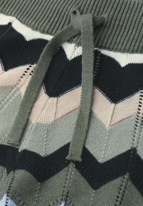 Close-up van een gebreid kledingstuk met chevronpatroon in groen, zwart en beige met trekkoordsysteem.