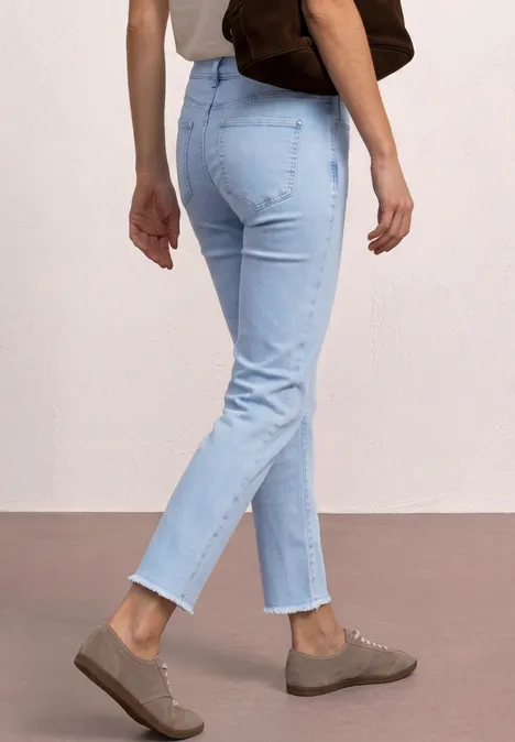 Person trägt helle Jeans, braune Slipper und eine Schultertasche vor hellem Hintergrund.