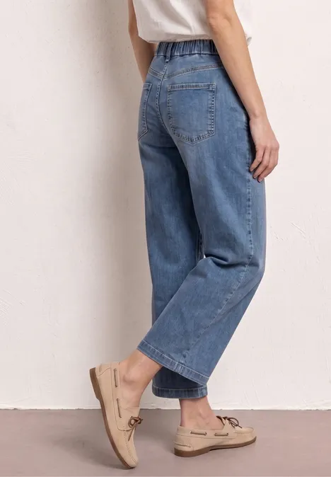 Vrouw in losse blauwe wijde jeans en beige loafers, zijaanzicht.