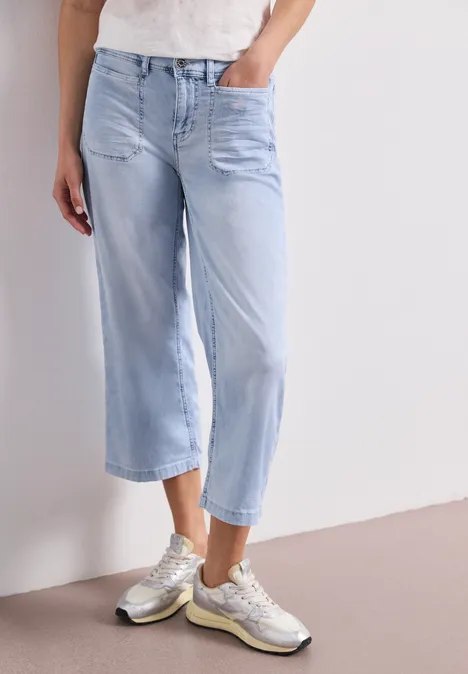 Helle, lässige weite Jeans in Cropped-Länge kombiniert mit silbernen Sneakern.
