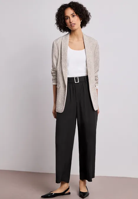 Eine Person trägt einen beigen Blazer, weißes Top und schwarze, weite Hose mit Gürtel.