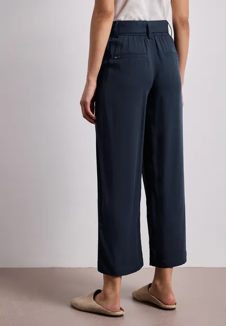 Rückansicht einer Person in marineblauer, weiter Hose mit Gürtelschlaufen und Taschen, kombiniert mit hellen Hausschuhen.