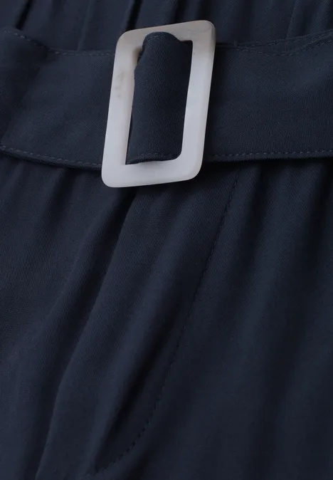 Nahaufnahme eines schwarzen Stoffgürtels mit silberner, rechteckiger Schnalle auf dunklem Stoff.