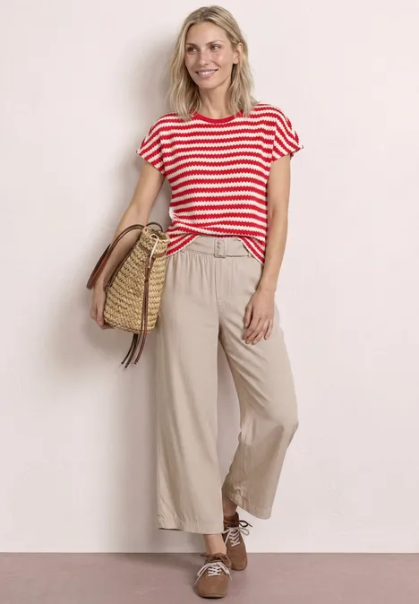 Frau in rot-weiß gestreiftem T-Shirt, beigen Culotte-Hosen und Strohtasche