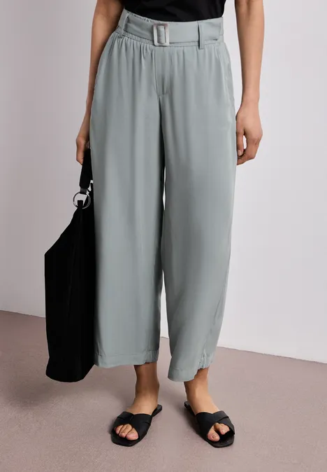 Graue, weite 7/8-Hose mit Gürtel, dazu schwarze Sandalen und schwarze Tasche.