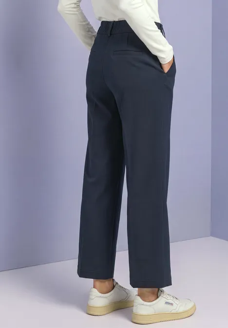 Personne vue de dos portant un pantalon large bleu marine, un haut blanc et des baskets blanches.