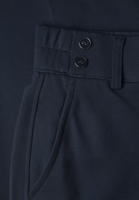 Gros plan d’un pantalon bleu foncé avec deux boutons, passants de ceinture et poche latérale.