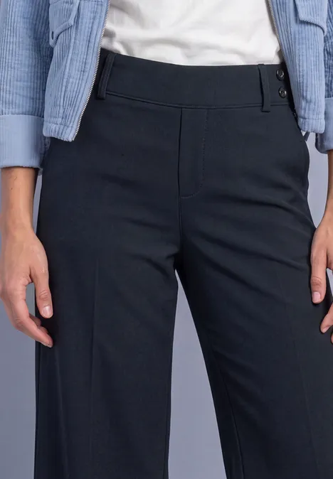 Femme portant un pantalon droit bleu foncé taille haute, t-shirt blanc et veste légère bleue.