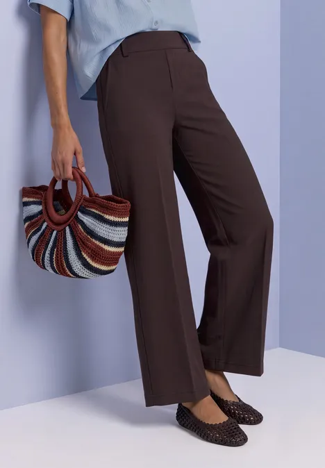 Femme en pantalon marron ample, chemise bleue claire, sac panier coloré et mocassins noirs
