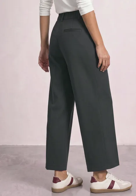Femme portant un pantalon ample gris et des baskets blanches à bande bordeaux.