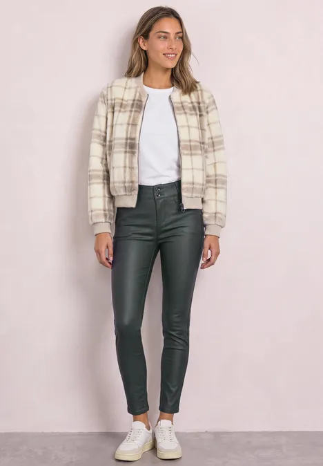 Frau in kariertem Hemdjacke, weißem T-Shirt, schwarzen Lederleggings und weißen Sneakern.